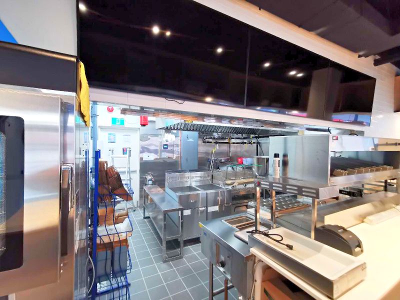 Stainless steel kitchen line with fryers and a grey tile floor