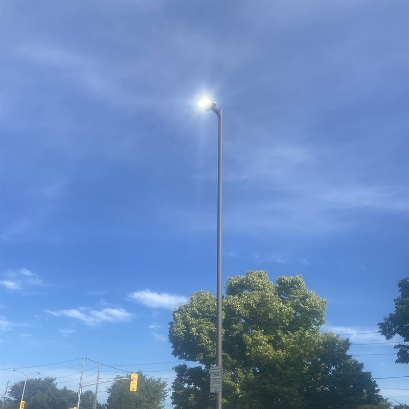 Tall parking lot pole with a bright LED area light against a blue sky
