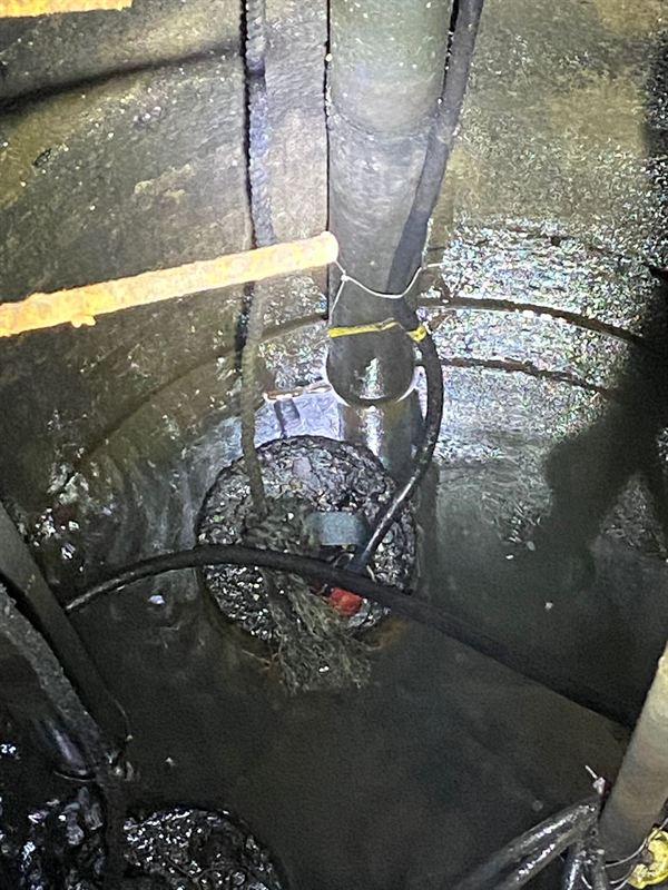 Looking down into a sanitary pump pit with the submersible pump, float cables and discharge pipe