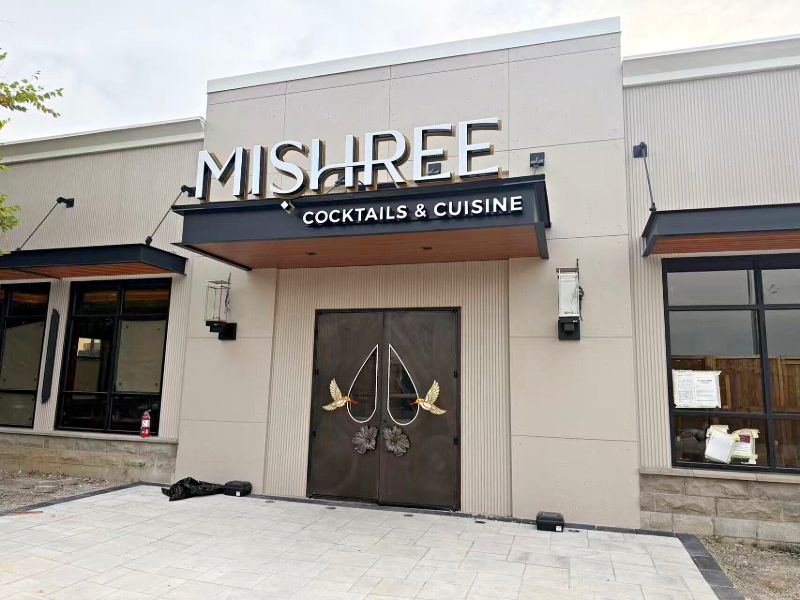 Restaurant storefront with a black canopy, lit sign and bronze double doors